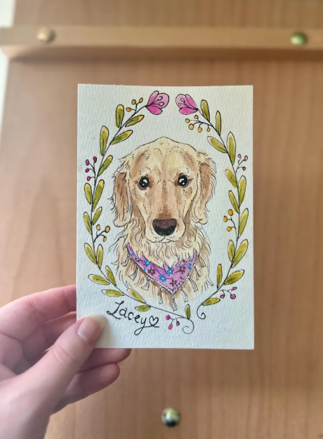 Card with a dog illustration and floral wreath held by a hand against a wooden background