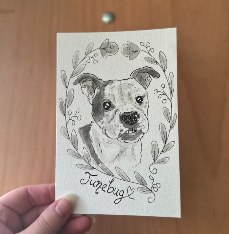 Hand-drawn card with a watercolor dog illustration and 'Junebug' text on a wooden surface.