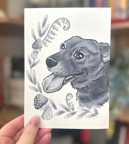A photo of a hand holding an illustration of a dog in black and white ink