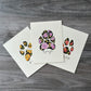 three small watercolor paintings of pet paw prints with colored flowers as a pattern