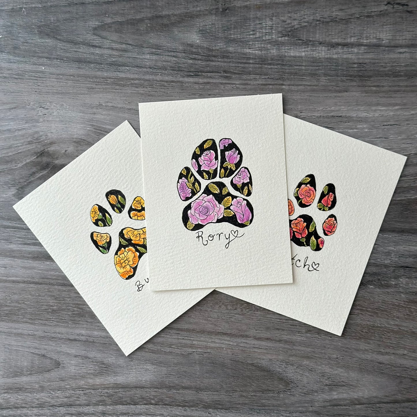 three small watercolor paintings of pet paw prints with colored flowers as a pattern