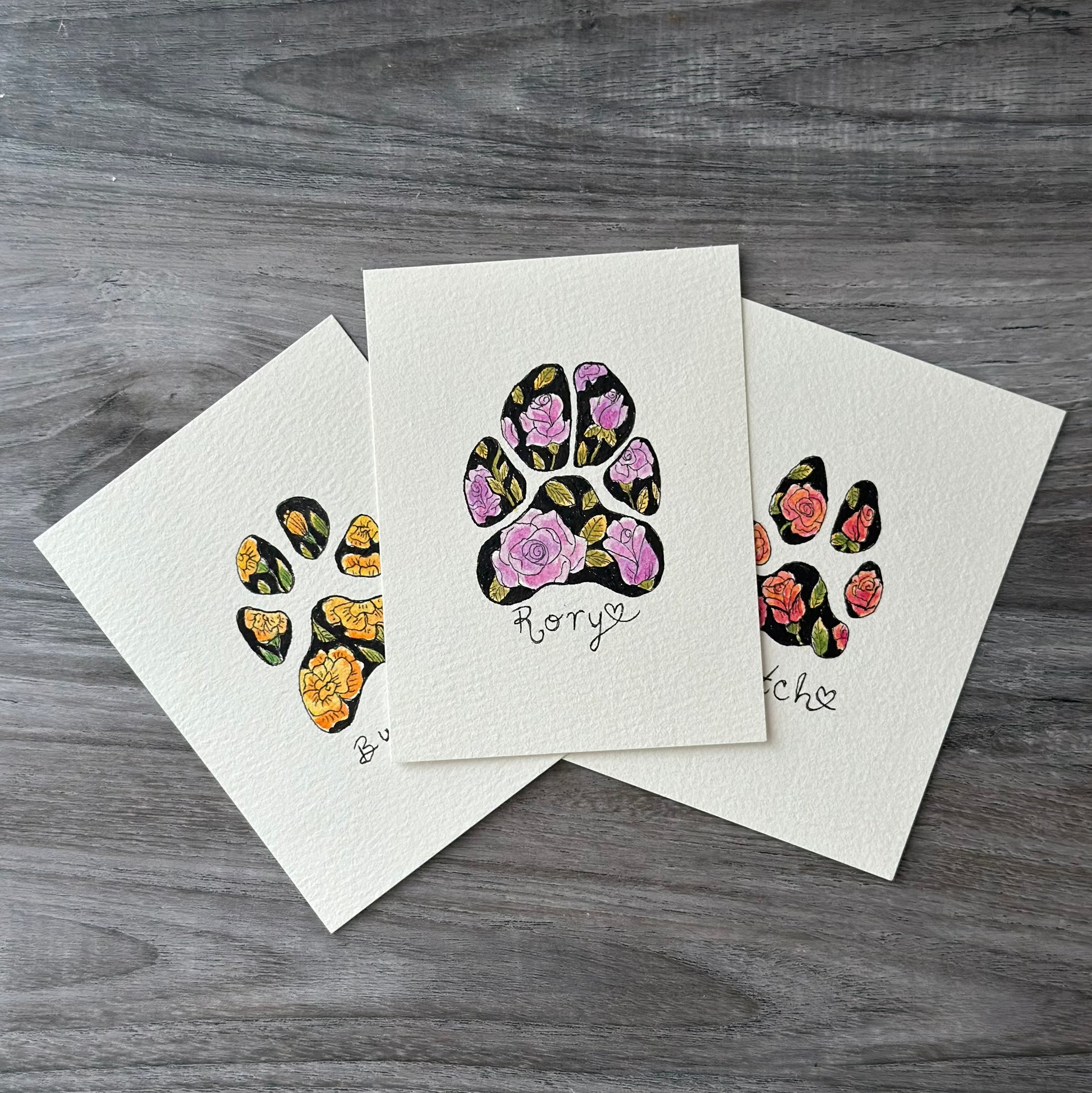 three small watercolor paintings of pet paw prints with colored flowers as a pattern
