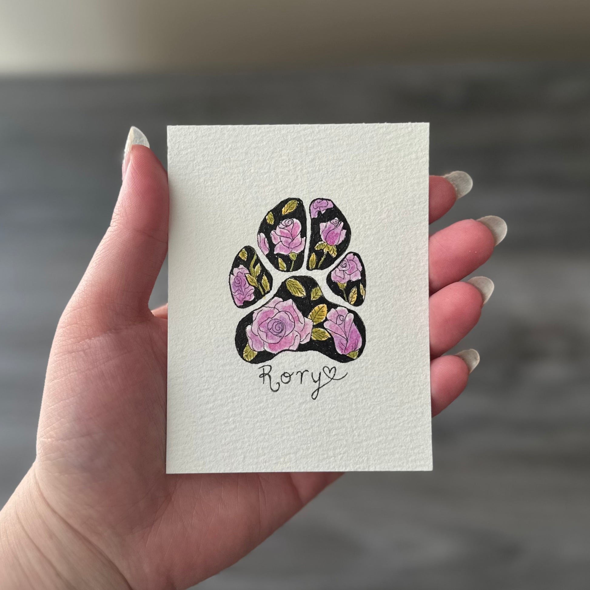 Hand holding a card with a floral paw print design and the name 'Rory'.