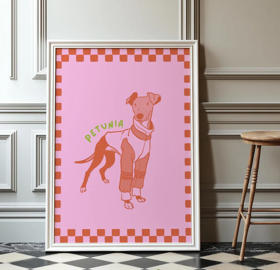 Framed artwork of a stylized line art dog illustration on a pink background and checkered boarder with 'Petunia' text, leaning against a wall.