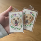 Two keychains with dog illustrations and names on a wooden surface.