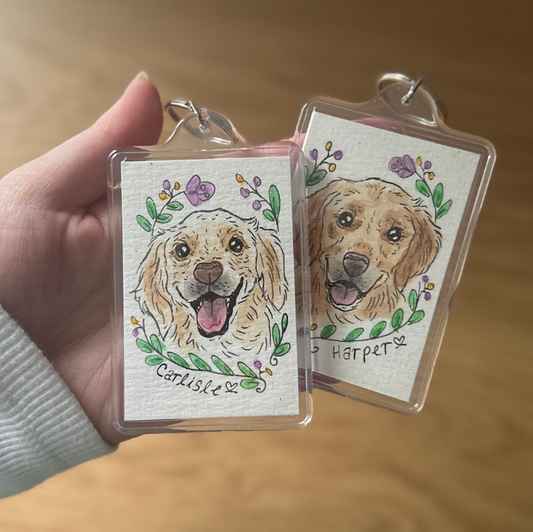 Two keychains with dog illustrations and names on a wooden surface.