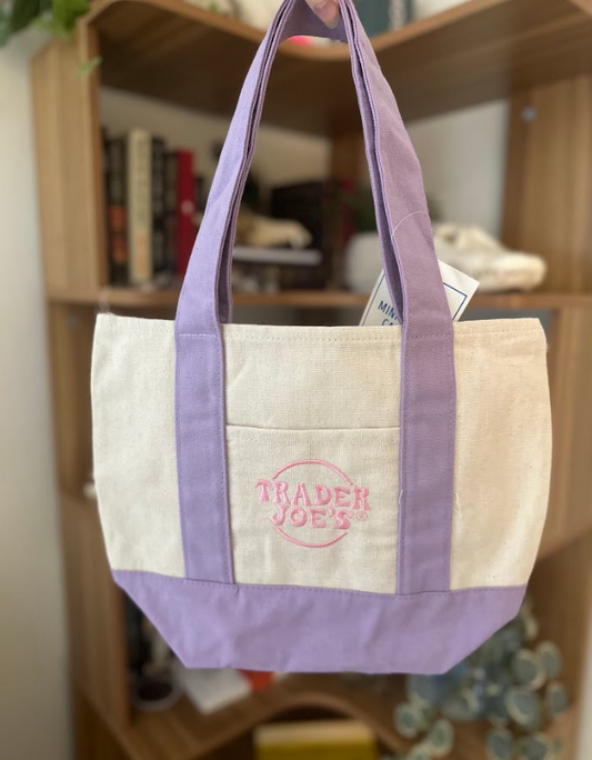 Tote bag with 'Trader Joe's' logo held in front of a bookshelf.