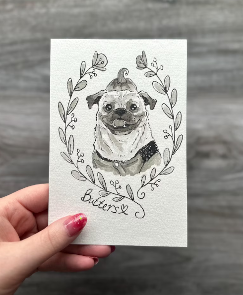 Hand holding a card with a pug illustration and 'Butters' text against a gray background