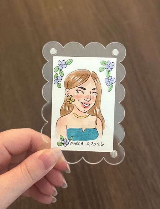 Hand holding a small card with a illustration of a woman and floral decorations on a wooden surface.