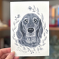 an image of a hand holding an illustration of a dog painted in black and white ink 