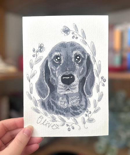 an image of a hand holding an illustration of a dog painted in black and white ink 