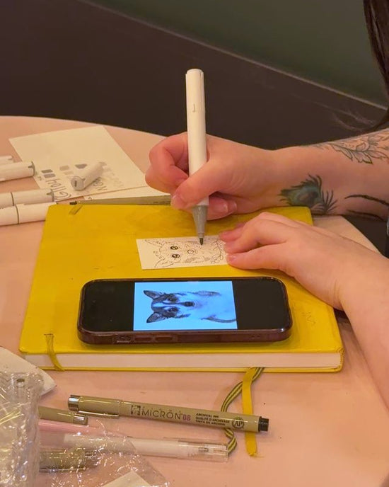 Person drawing on a notebook with a smartphone displaying a dog image